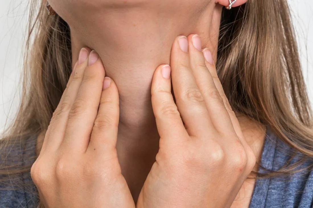 A woman touching the front of her neck with both hands